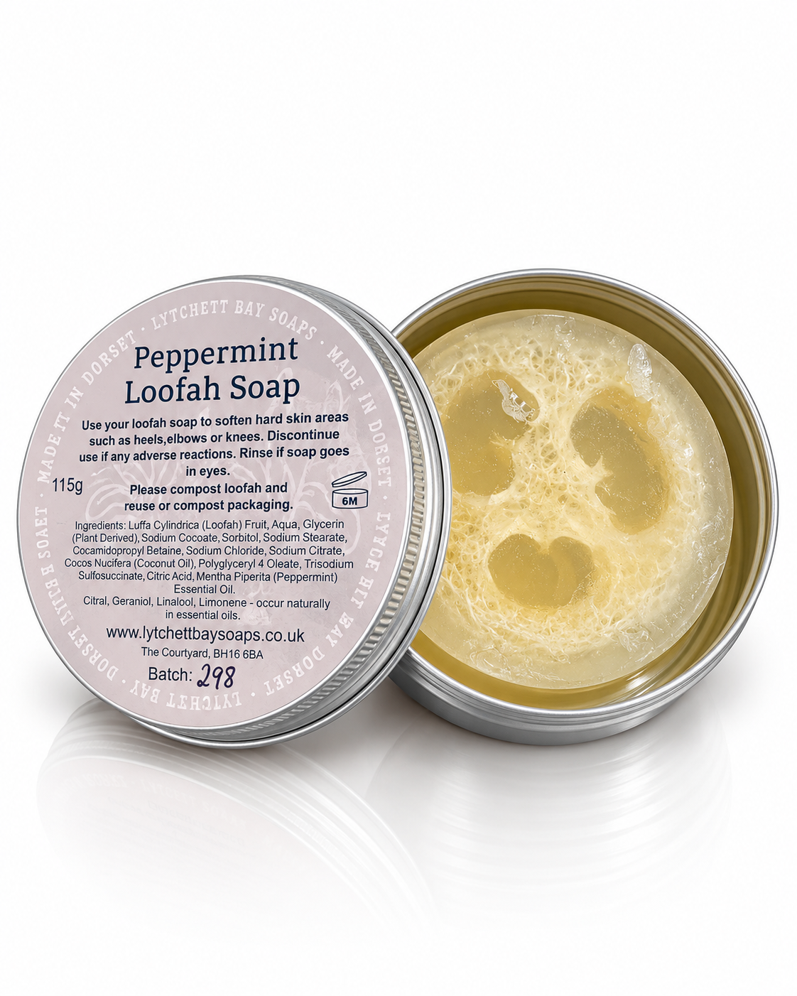 An open round metal tin of Peppermint Loofah Soap by The Clunyhouse Soaps, showing the pale yellow soap inside, with the lid placed beside it on a white reflective surface.