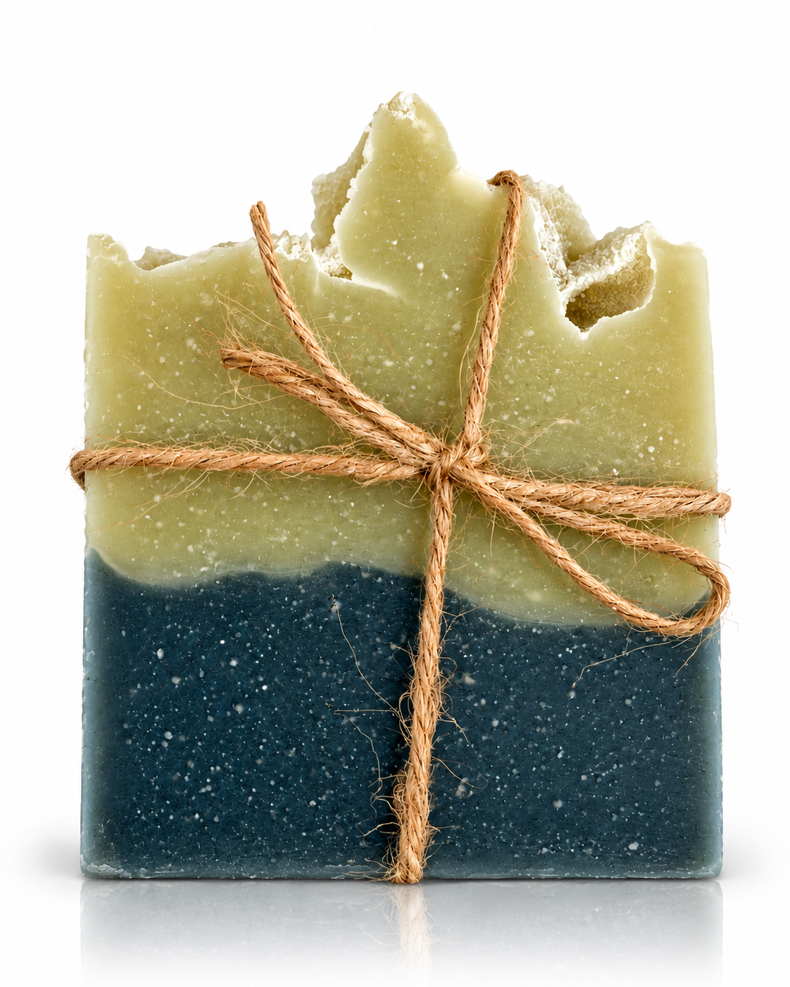 A handmade rectangular bar of soap with a rustic, broken top edge, featuring a two-tone design with a light olive green upper half and a dark blue speckled lower half, wrapped in a natural jute twine bow against a white background.