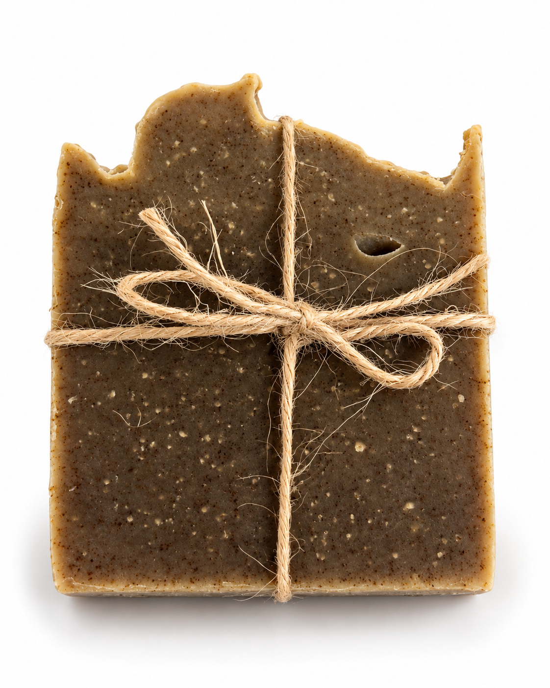 A rustic, hand-crafted rectangular soap bar with irregular, broken edges, wrapped in natural jute twine tied in a bow. The soap has a speckled, earthy brown color with tiny flecks of white and dark brown, set against a clean white background.